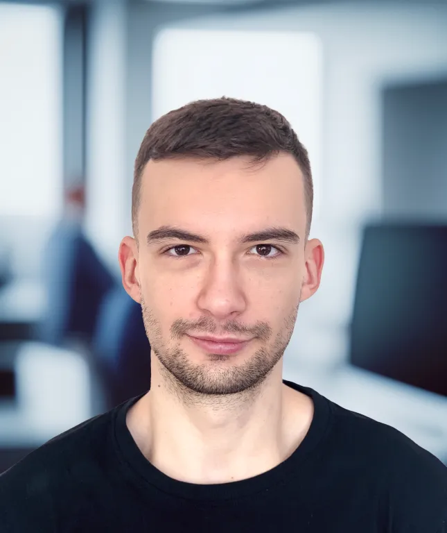 Michal in a black t-shirt stands in an office environment